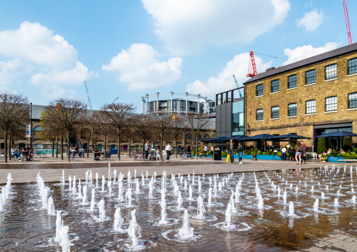 The Kings Cross development, with members of the public and a water fountain in the foreground.