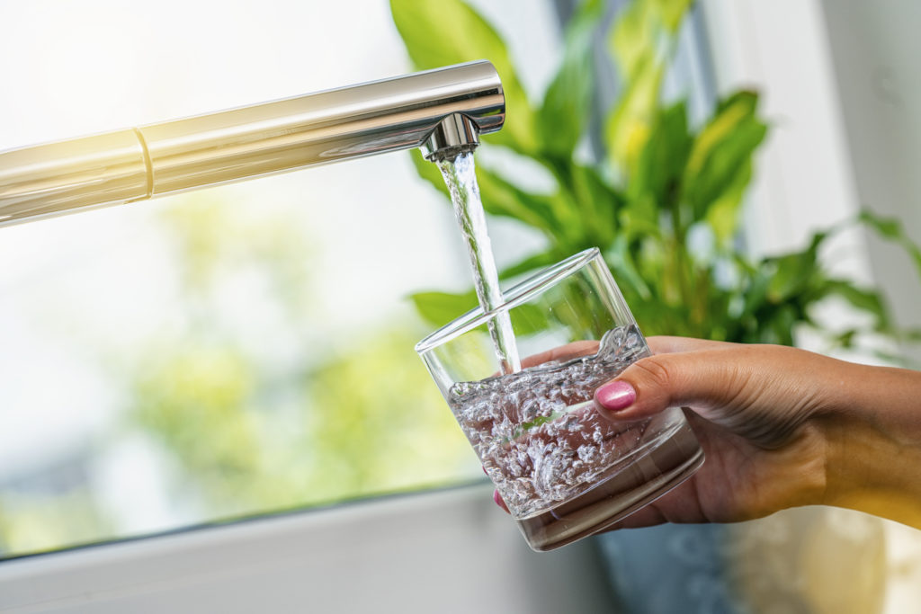 A hand holding a glass under a kitchen tap, filling it with water.