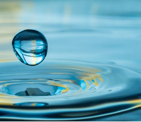 Close up of a water droplet above the surface of a larger body of water.