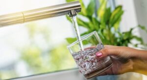 A hand holding a glass of water, which is being filled up under a tap.