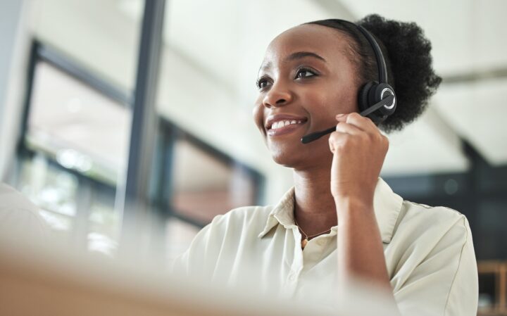 An image of a woman working in a contact centre, wearing a headset taking a call from a customer.